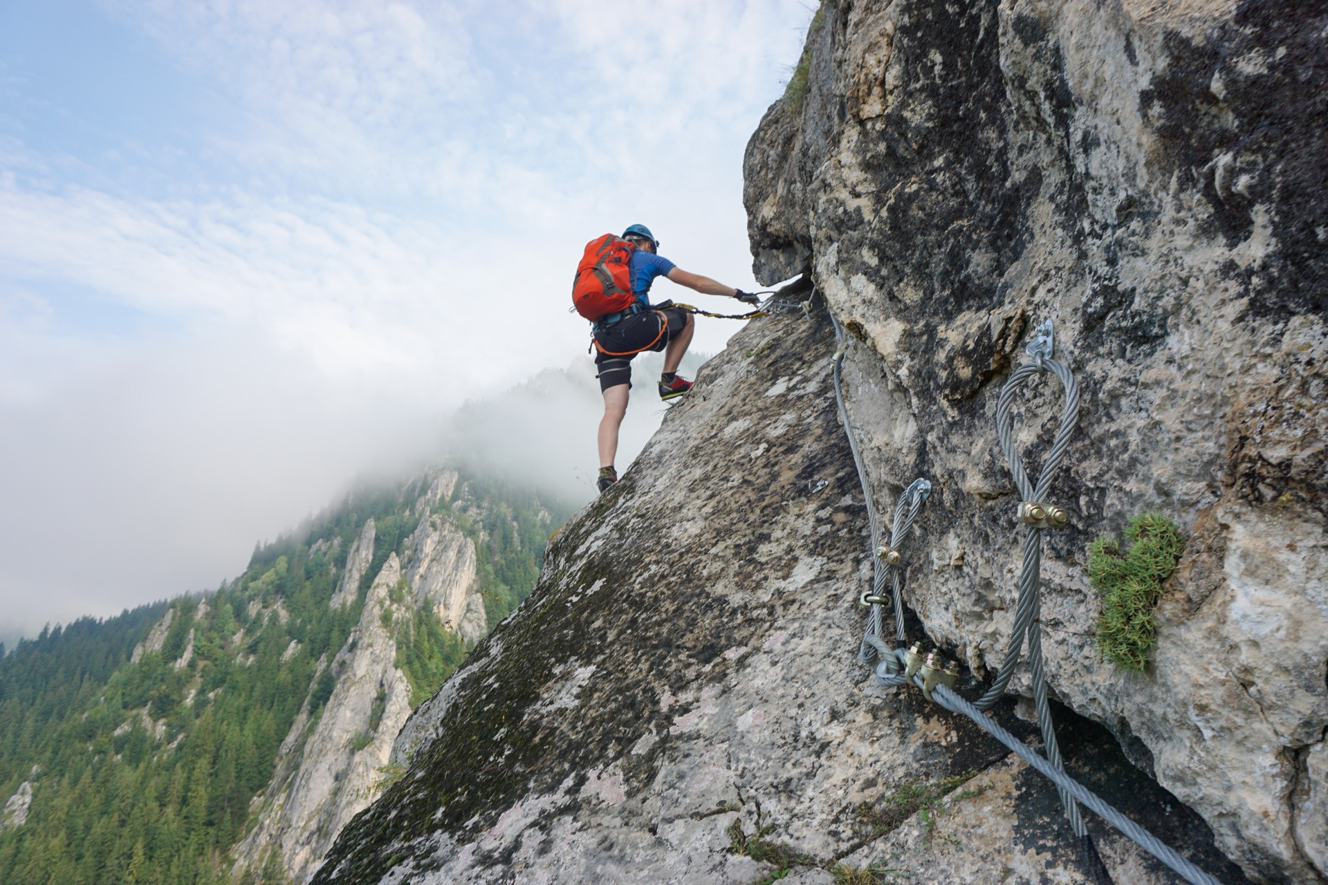 Klättrare med hjälm på en via ferrata med stålvajer i brant klippvägg