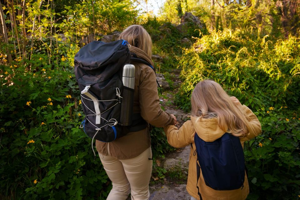 Vuxen och barn med ryggsäckar går hand i hand på en skogsstig